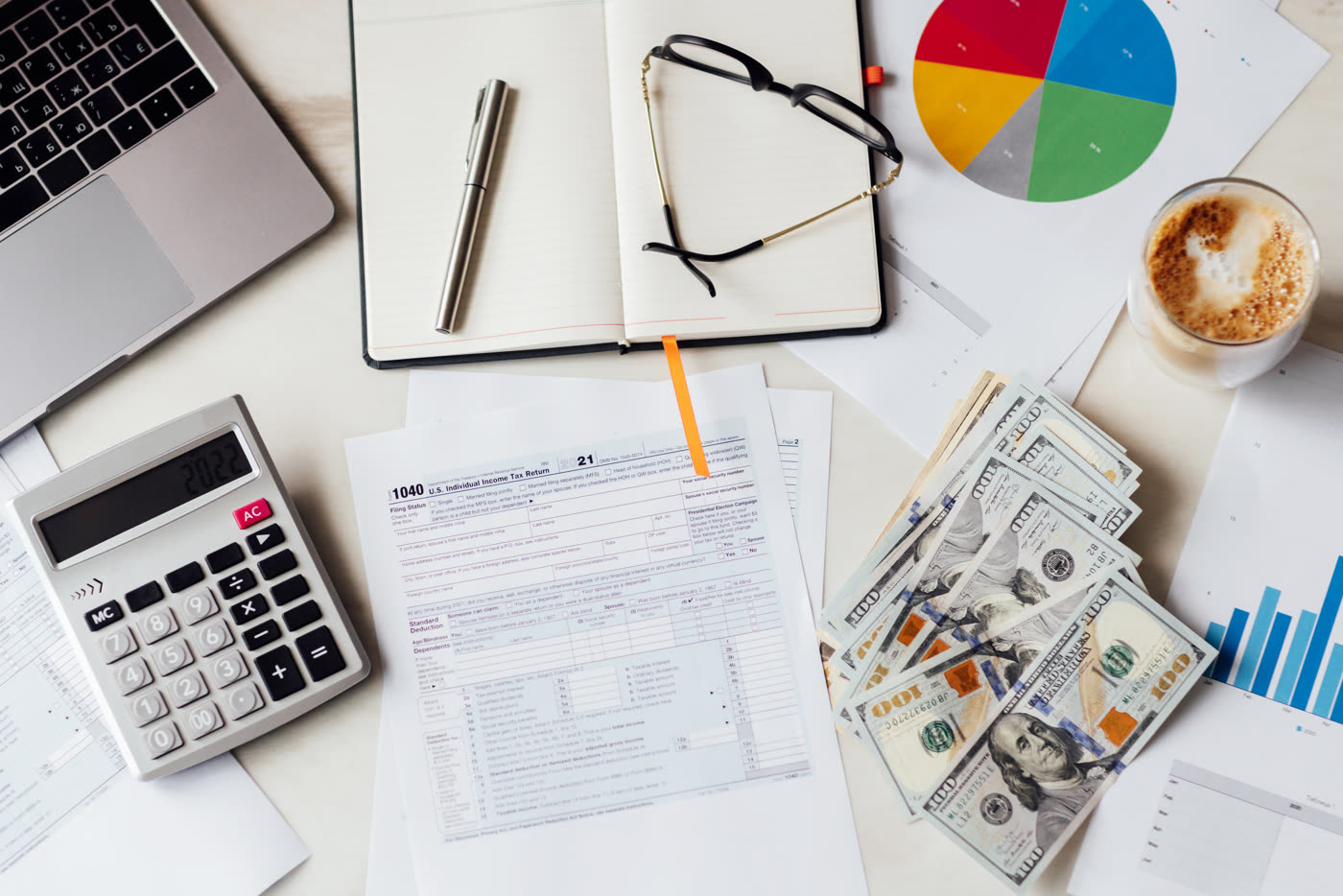 A desk with a laptop, notebook, pie chart and bank notes