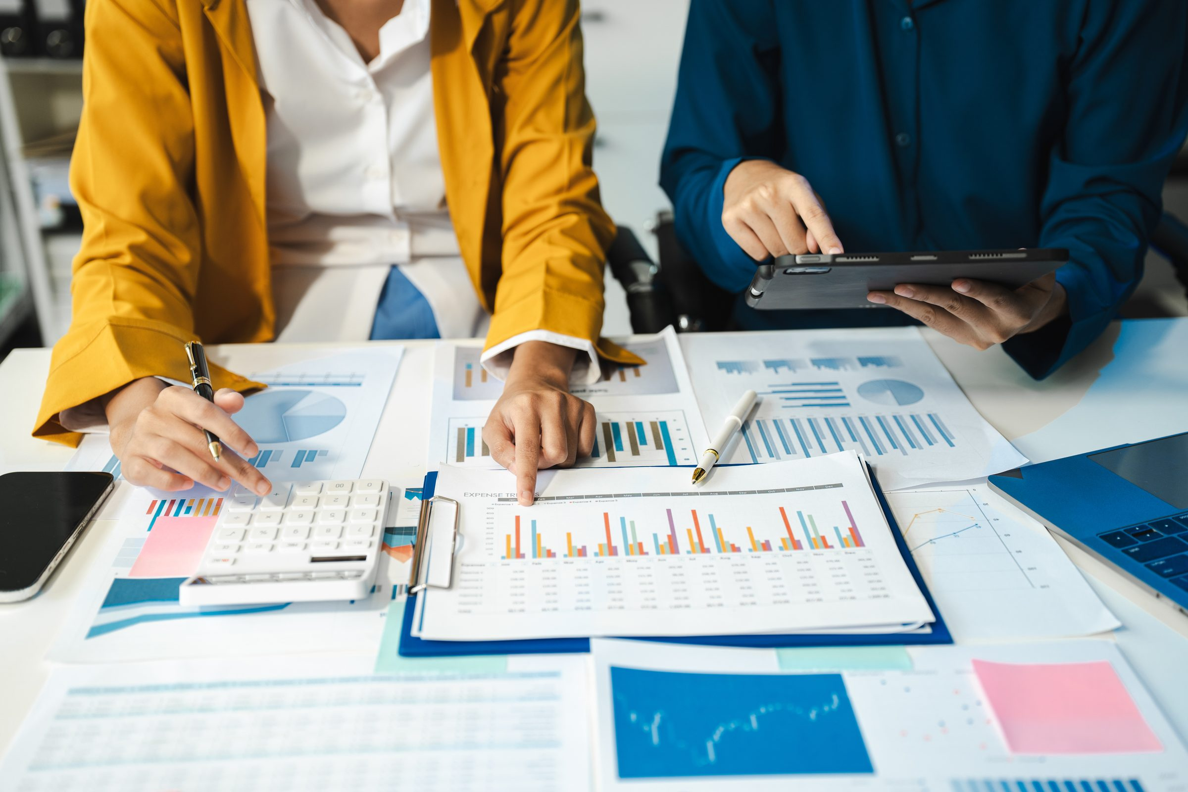 Two colleagues reviewing printed expense reports and charts, one holding a tablet