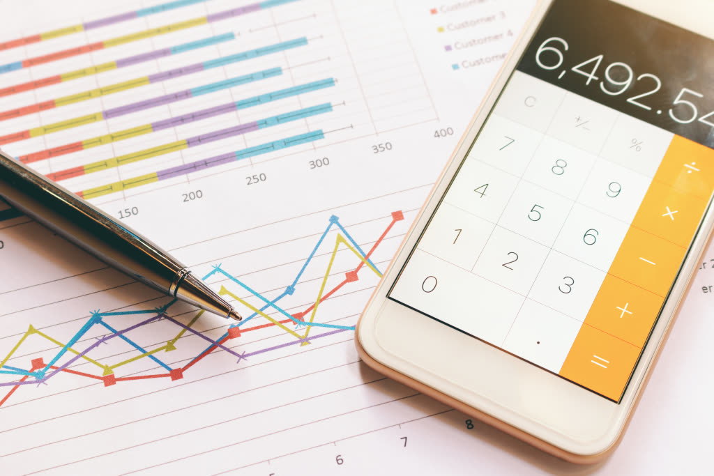 A phone calculator resting on printed financial charts and a pen