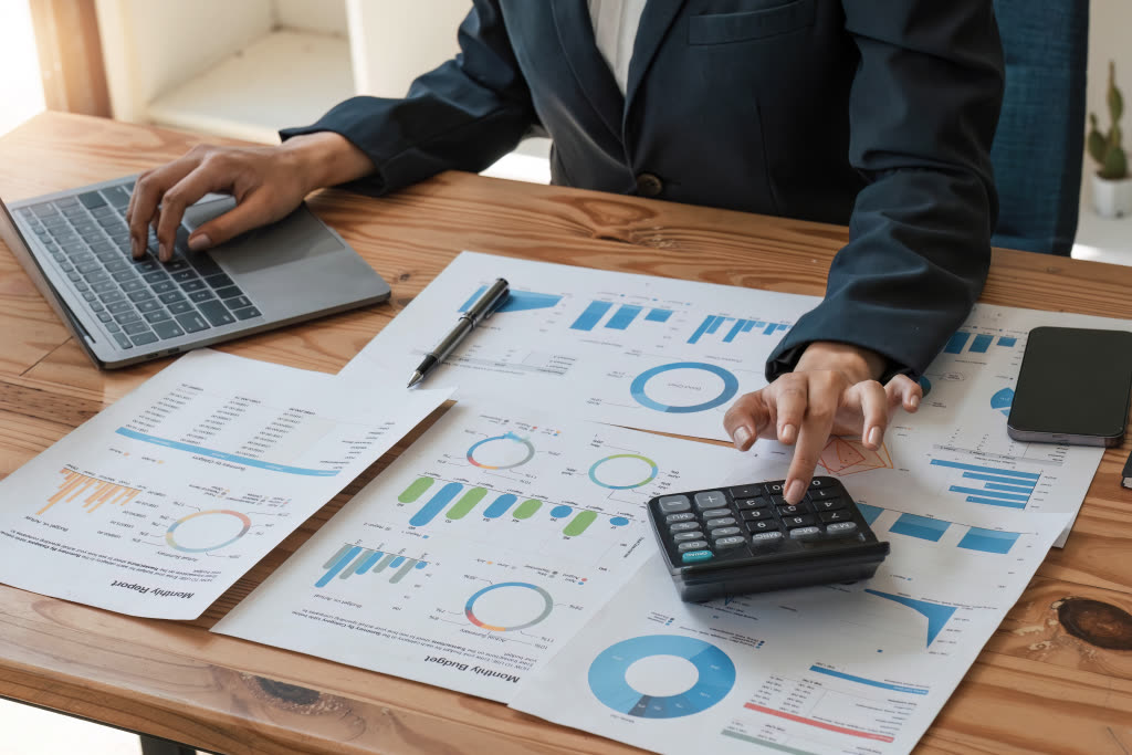 Hands working across a laptop and printed financial charts