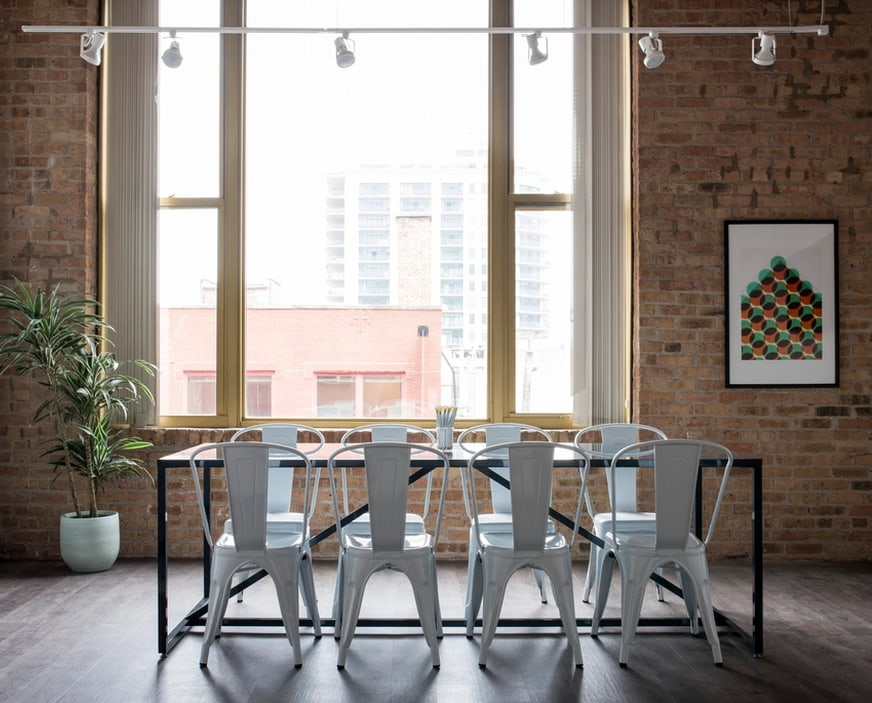 A meeting table and chairs by the windows of a brick-walled office